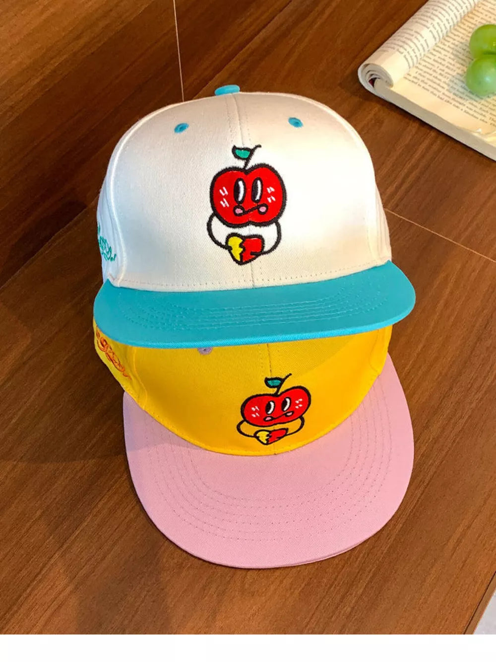 Baseball cap with embroidered apple graphic, featuring a white crown and teal brim.