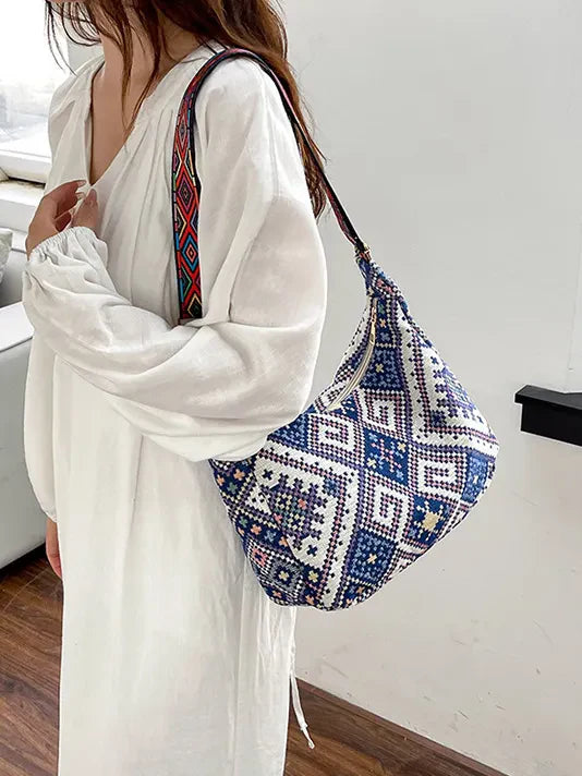 Embroidered geometric hobo bag in blue with a colorful woven strap.