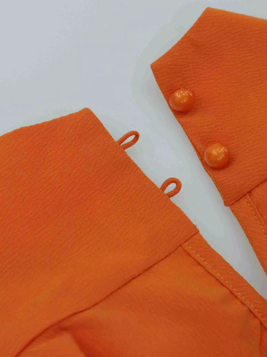 Tangerine halter mini dress detail with criss-cross straps and decorative buttons.