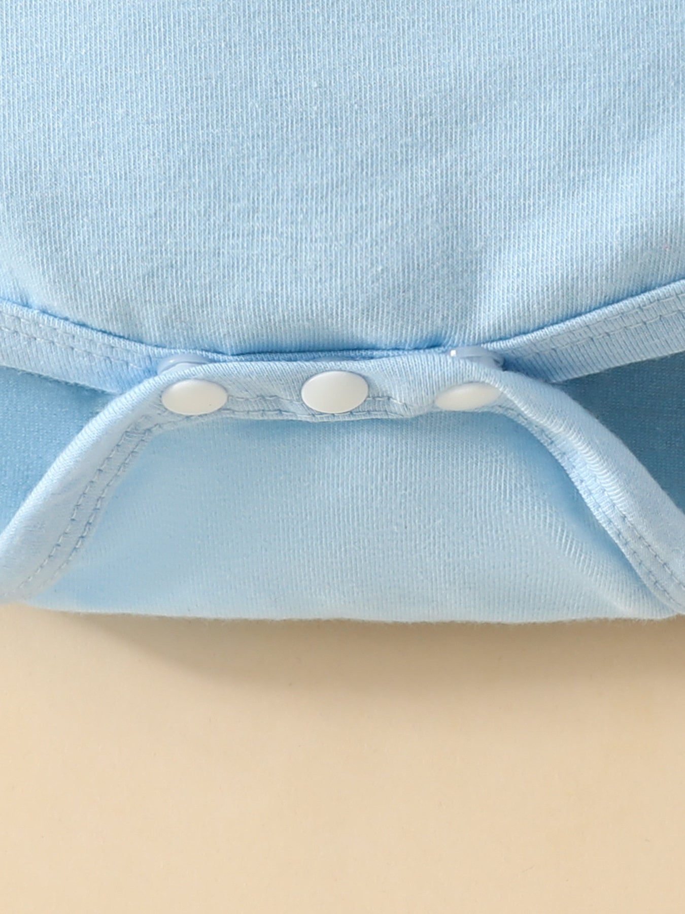 Light blue baby bodysuit detail showing white snap closures and ribbed trim.