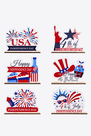 Patriotic wooden tabletop decor with USA, Statue of Liberty, cakes, bottle, hat, and fireworks designs.