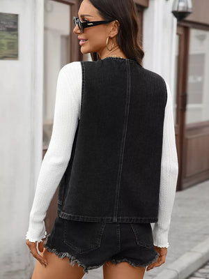 Black denim vest with button-down front and pockets, collarless, worn over a white sweater.