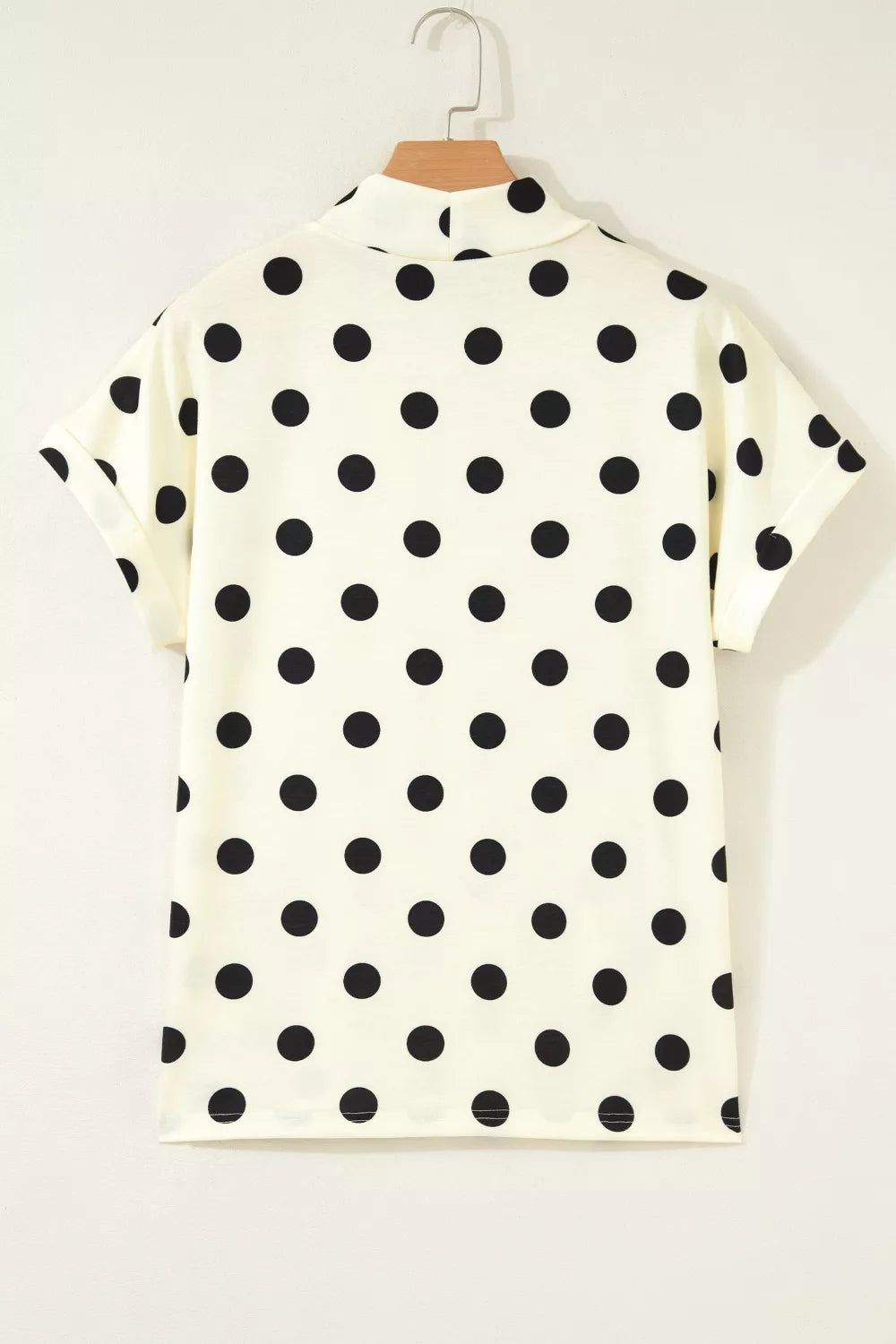 Cream polka dot short sleeve shirt with a mock neck and cuffed sleeves.