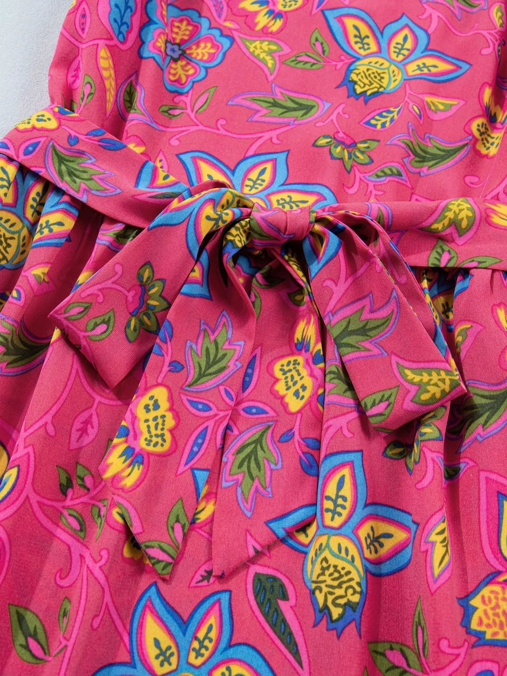 Belted floral midi dress in cotton blend with a pink background and vibrant blue, yellow, and green print.