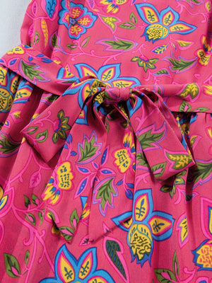 Belted floral midi dress in cotton blend with a pink background and vibrant blue, yellow, and green print.