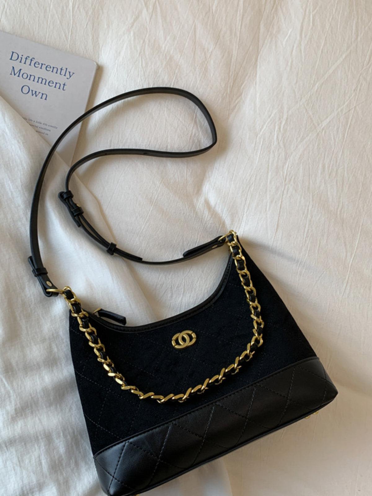 Black half-moon crossbody bag with gold chain and quilted leather trim.