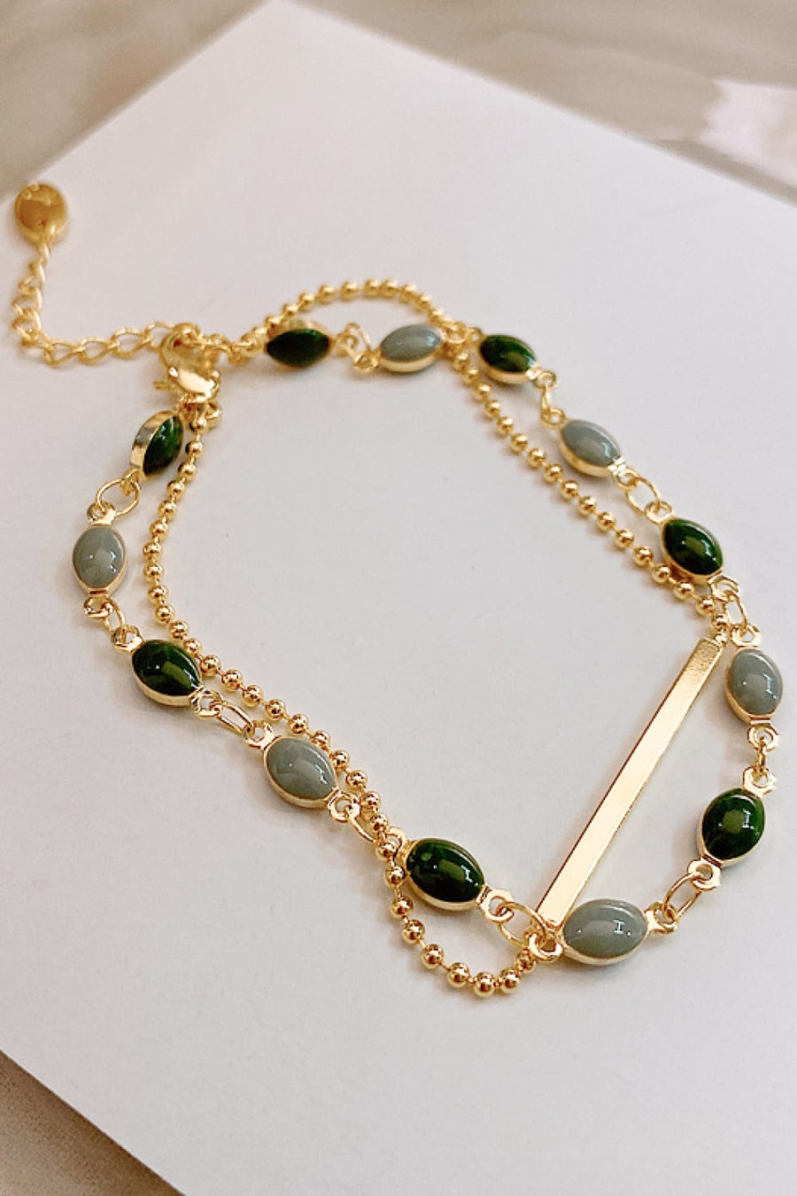 Gold dual chain bracelet with green and grey oval stones and a bar accent