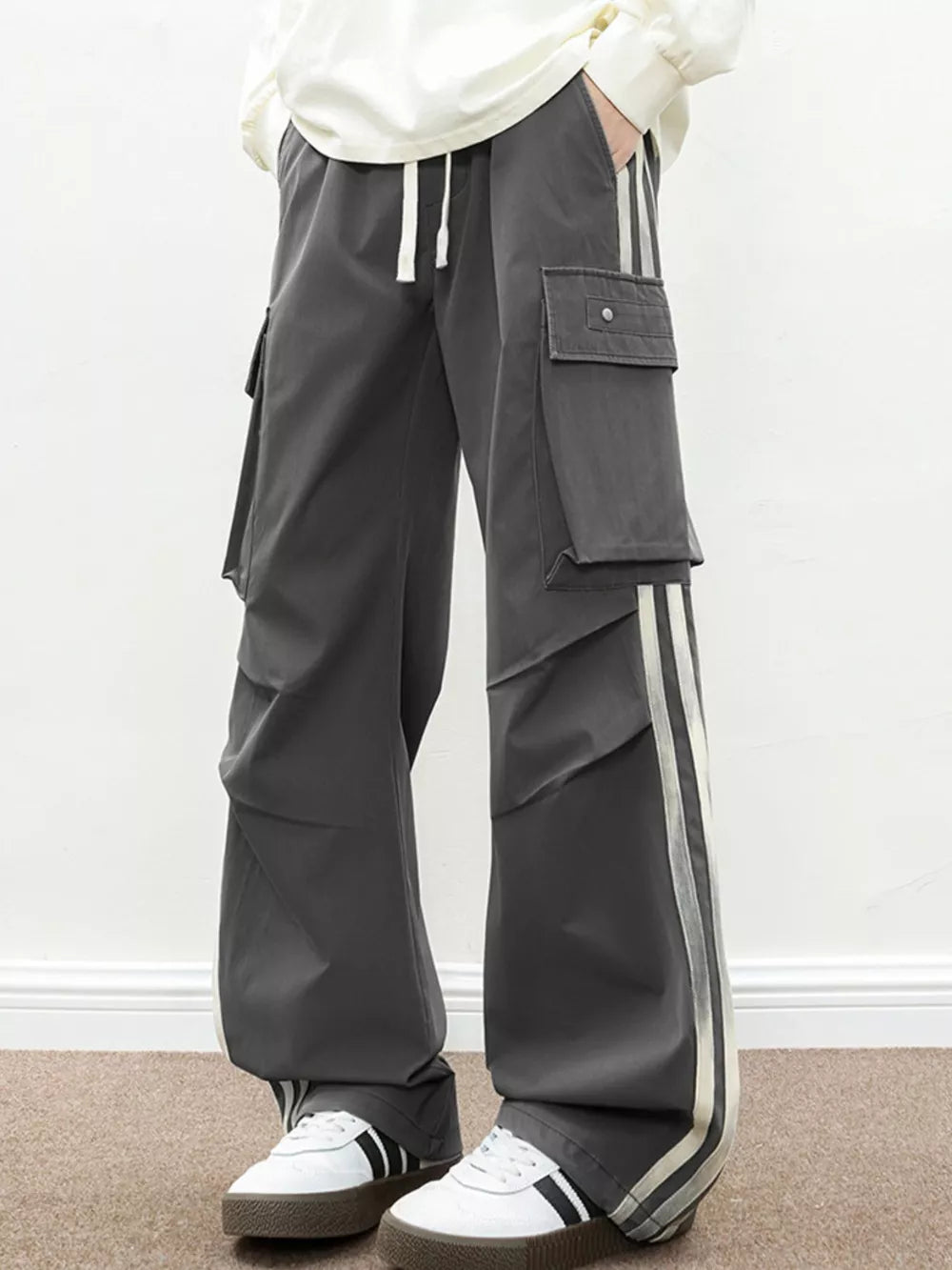 Oversized dark gray cargo pants with flap pockets and side stripes.