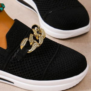 Black mesh slip-on flats with a chunky gold chain detail and white sole.