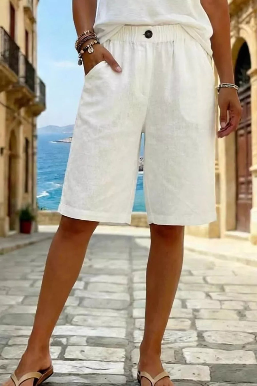 White pocketed knee-length shorts with elastic waist and button detail.