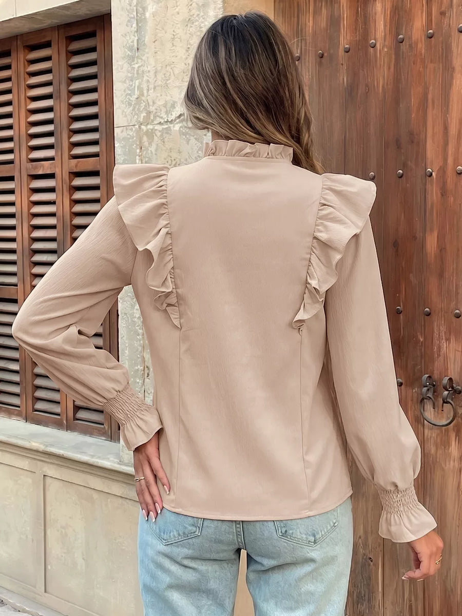 Chic beige long sleeve shirt with ruffled shoulders and cuffs, mock neck, and smocked wrists.
