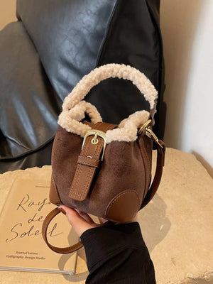 Brown suede bucket bag with fuzzy trim and gold buckle detail.