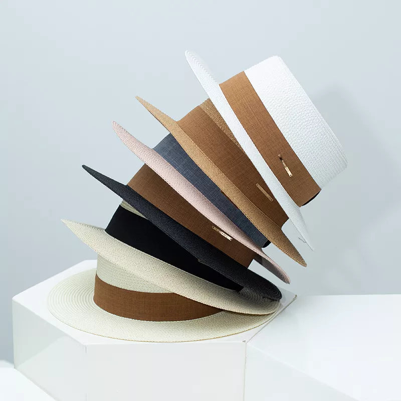 Woven straw boater hats in ivory, pink, white, black, khaki, and beige, each with a ribbon band.