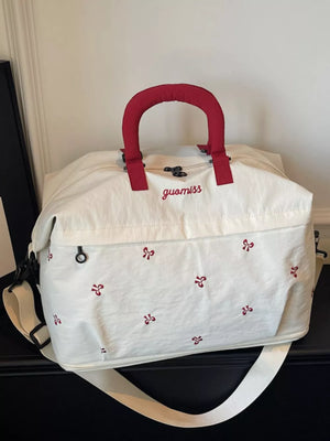 White duffel bag with red bow embroidery and red padded handles.