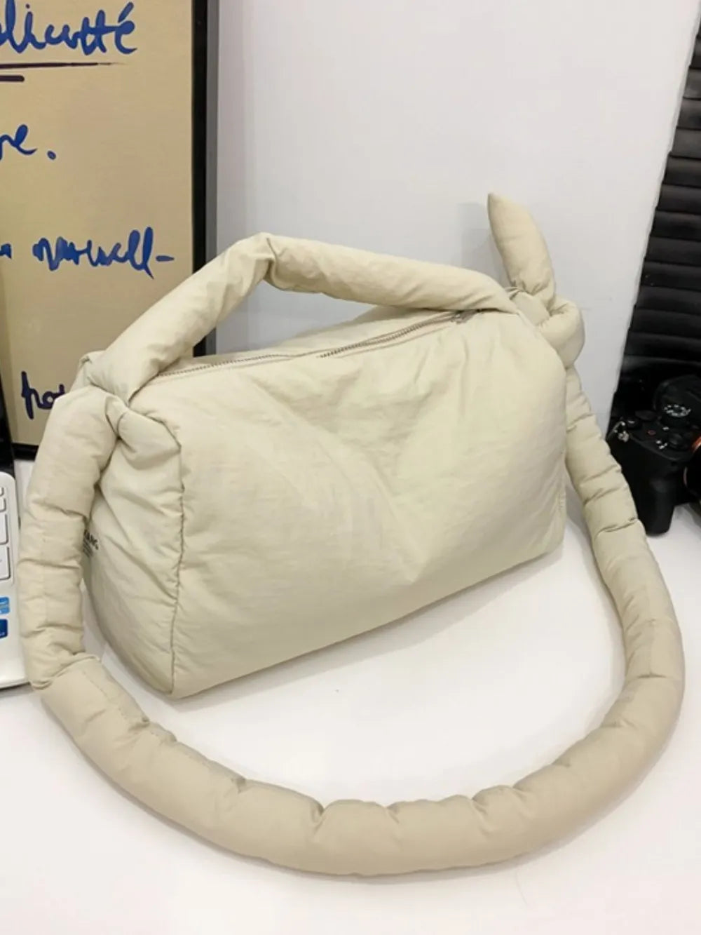 Beige padded knot shoulder bag with a zipper closure and a long knotted strap.