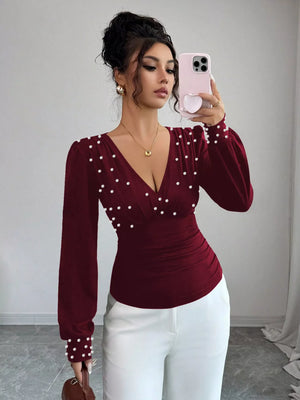 Burgundy ruched V-neck blouse with pearl embellishments and long sleeves.