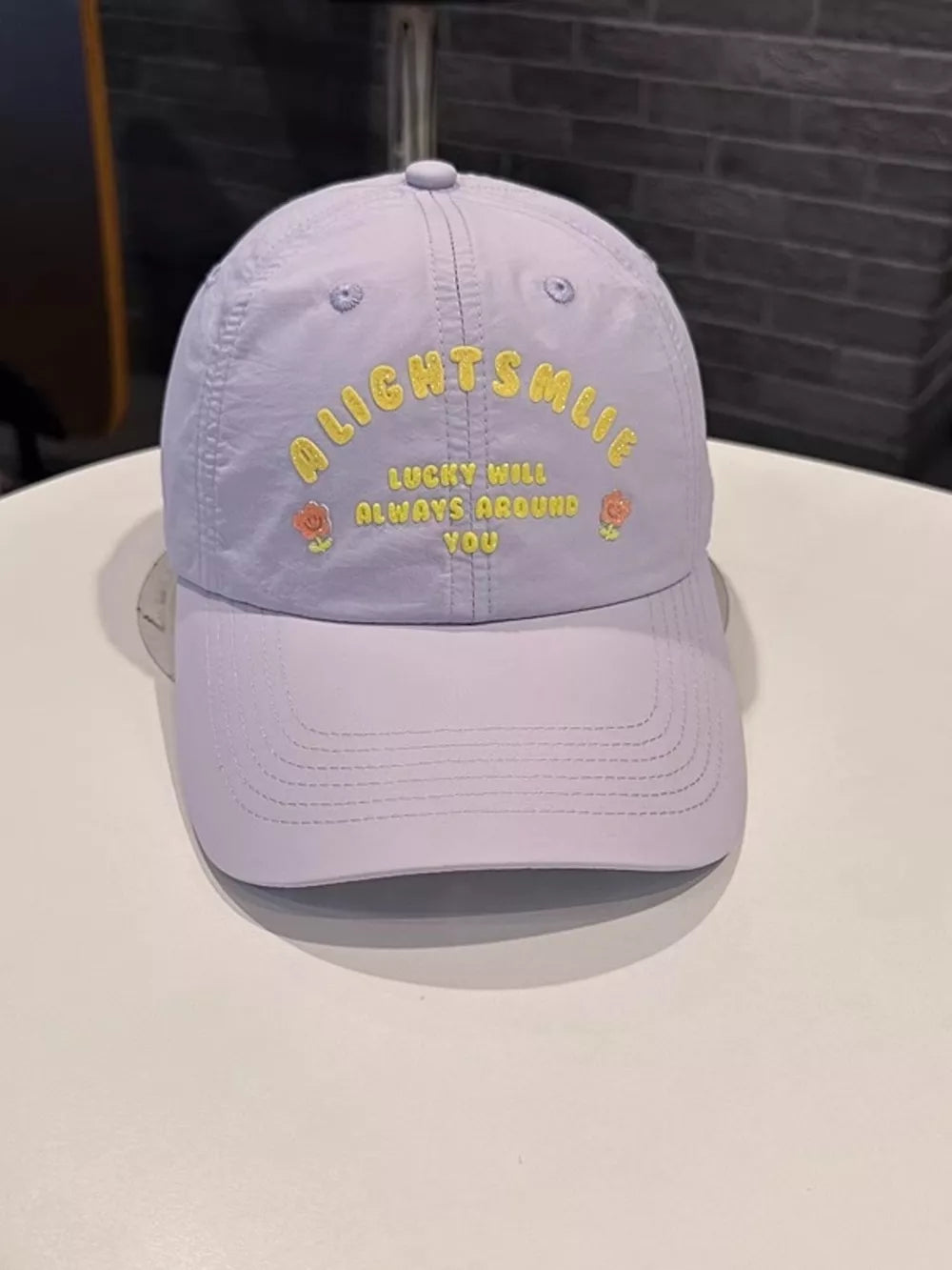 Lilac baseball cap with yellow text and rose embroidery.