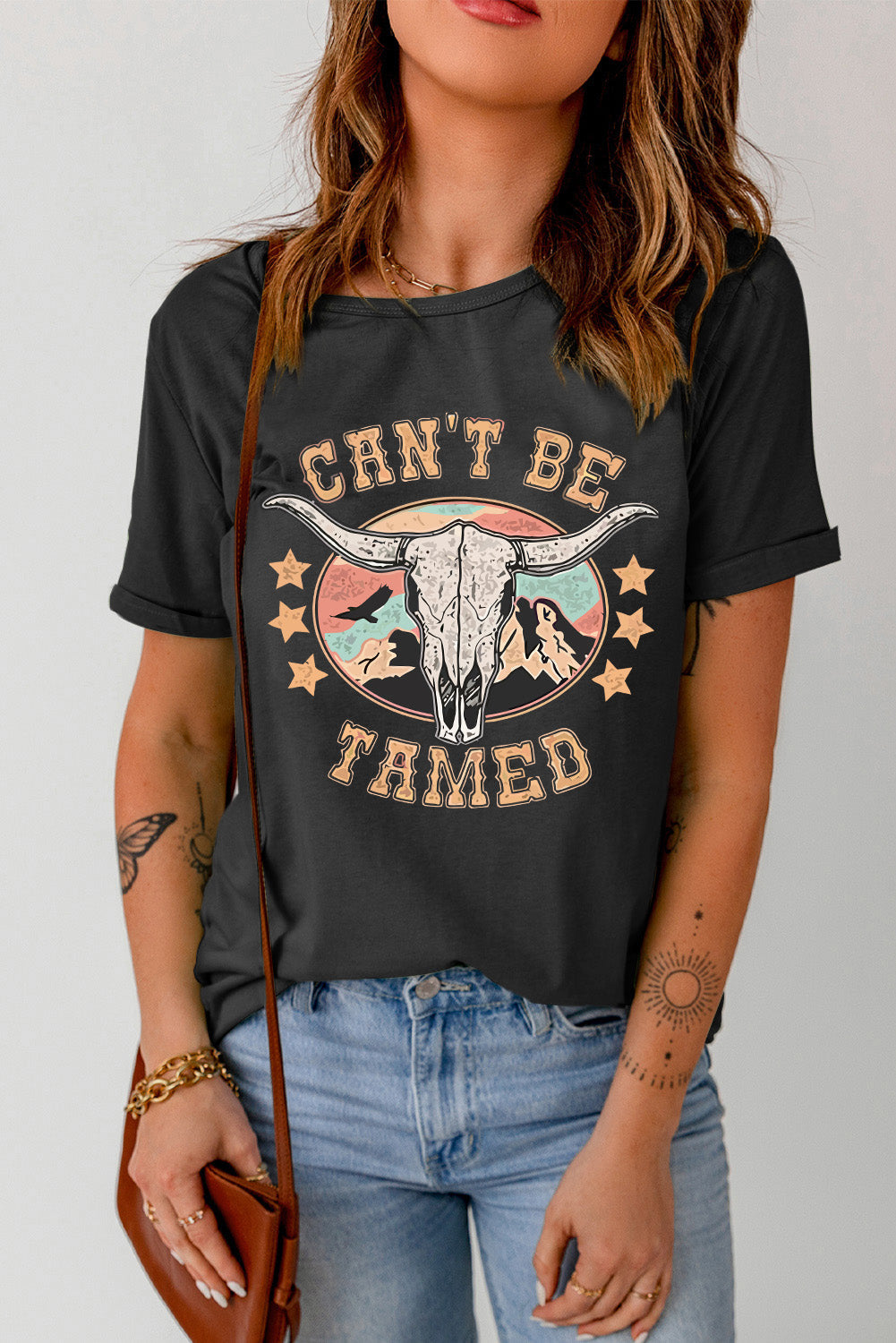 Black graphic t-shirt with a bull skull and mountains design, "Can't Be Tamed" text.