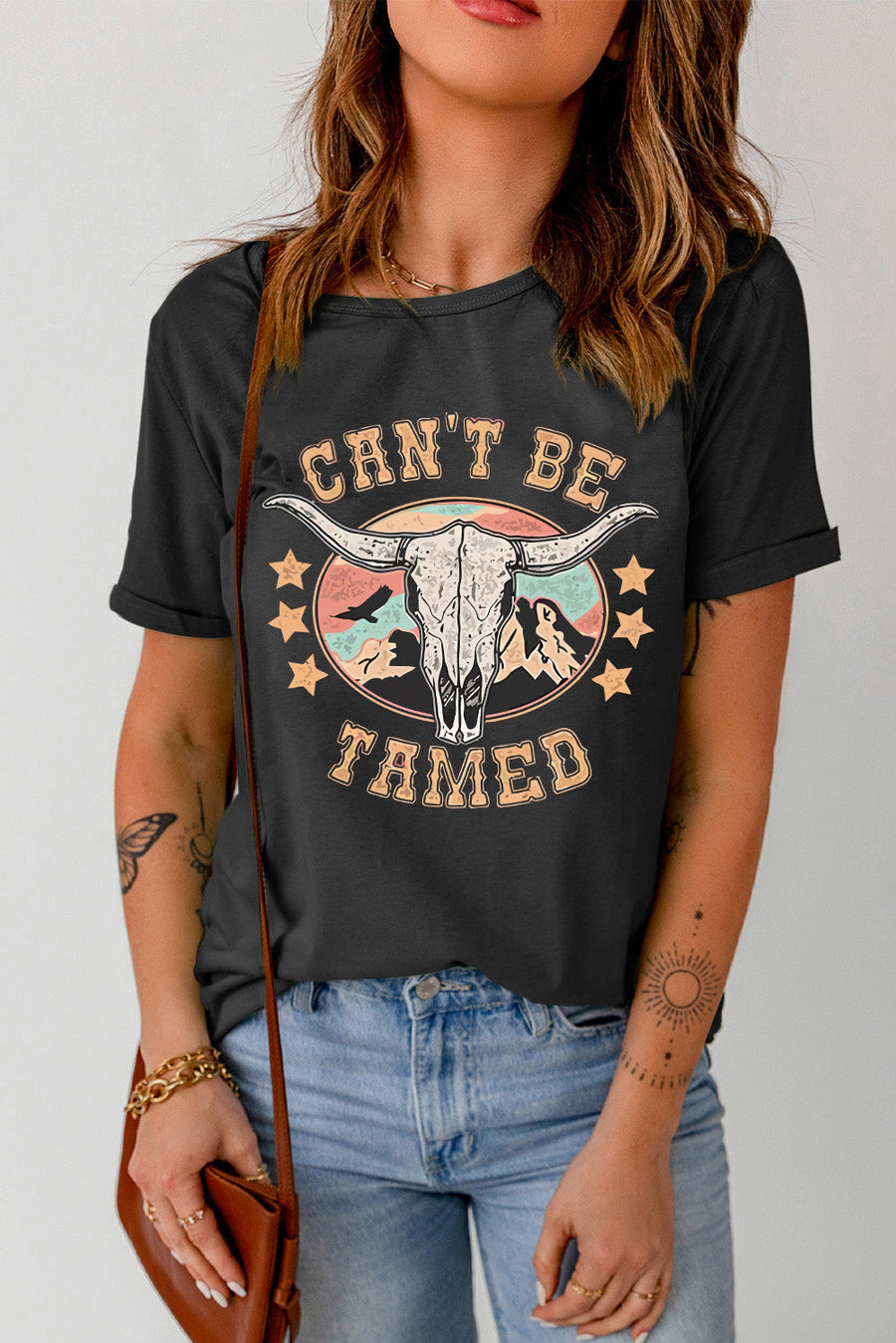 Black graphic t-shirt with a bull skull and mountains design, "Can't Be Tamed" text.