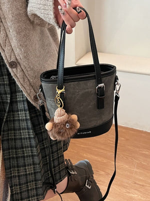 Premium two-tone bucket crossbody bag in gray with black trim and a fuzzy pompom charm.
