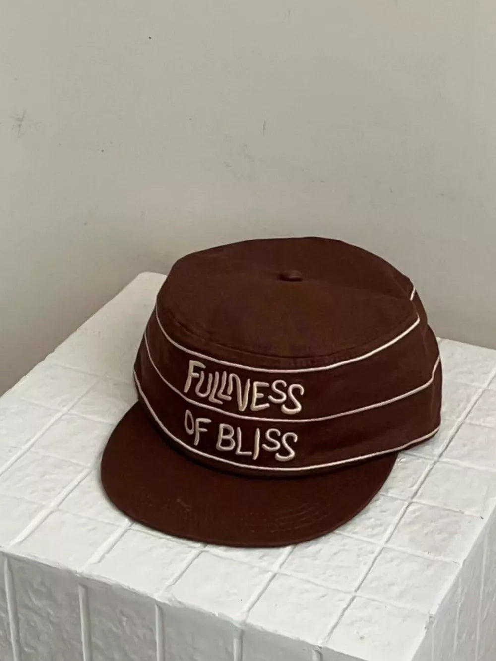 Brown cotton baseball cap with white embroidered slogan Fullness of Bliss and piping detail.