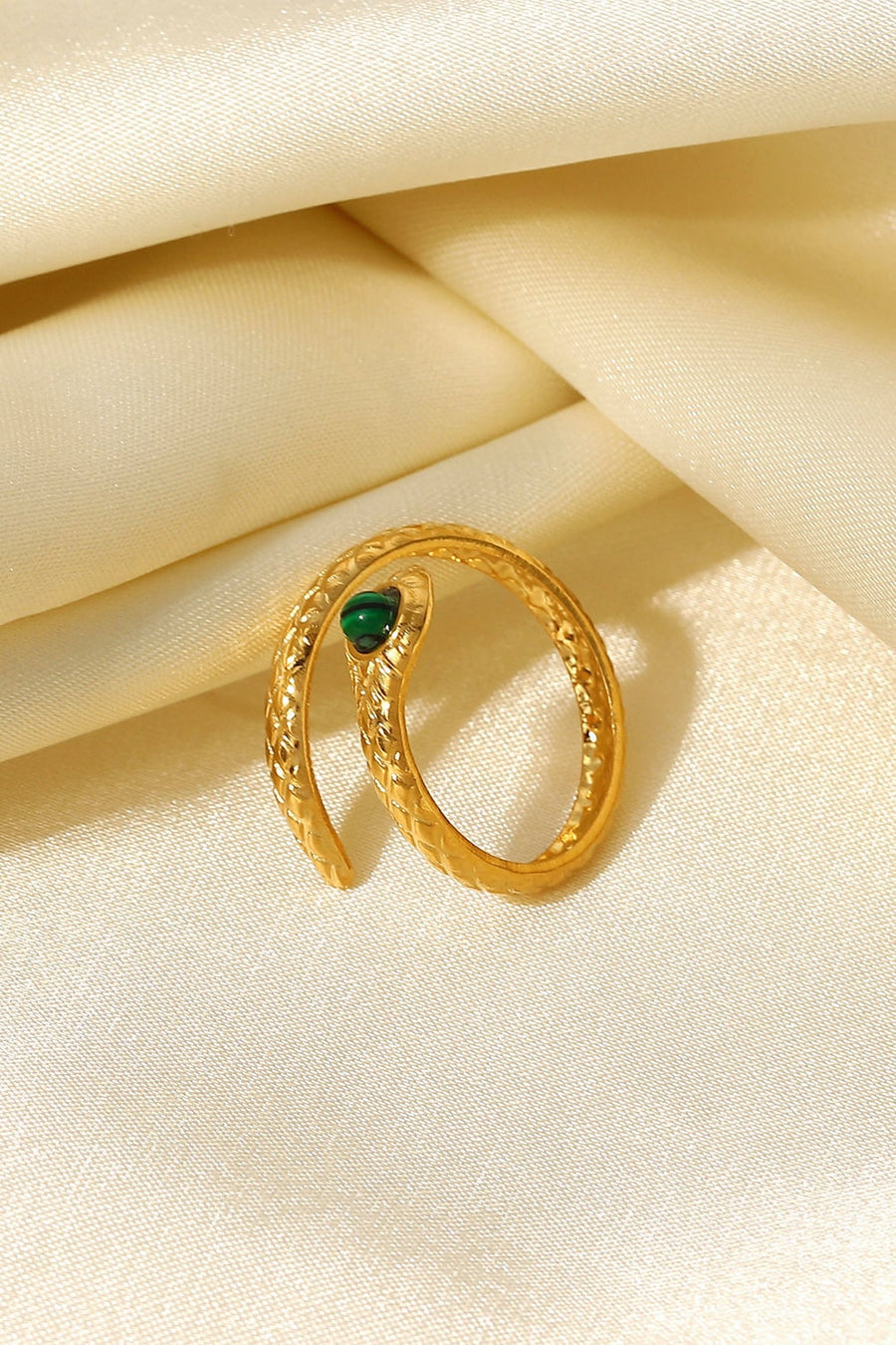 Gold serpentine ring with malachite eye detail and textured coil design.