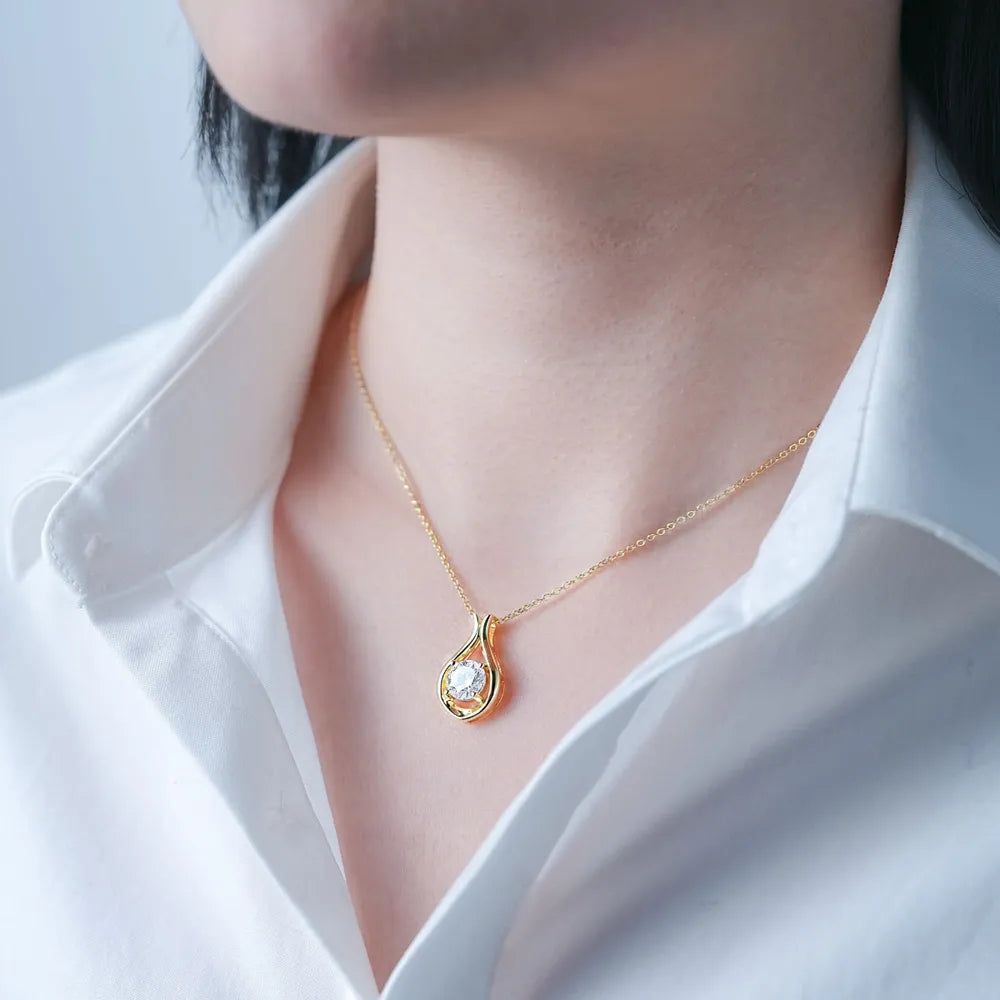 Gold teardrop pendant necklace with moissanite stone on a woman wearing a white shirt.