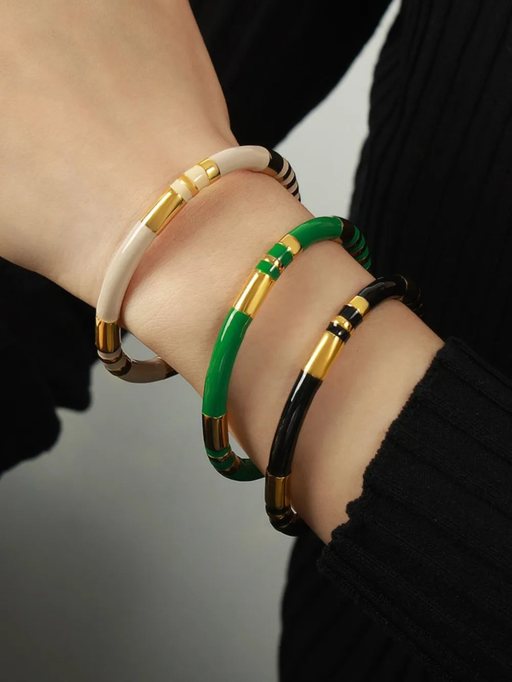 Striped enamel and gold bangles in dark green, black, and cream, stacked on a wrist.