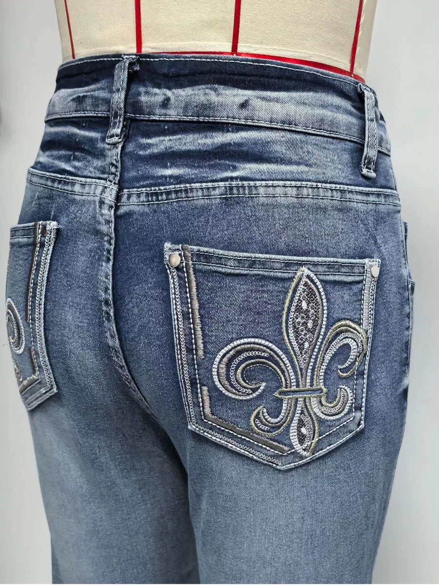 Classic high-waisted flare jeans in blue denim with ornate embroidered fleur-de-lis back pockets.
