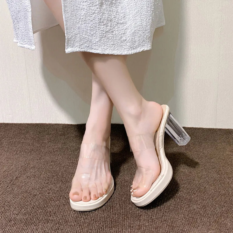 Lucite heel platform slides in beige with clear straps and a chunky transparent heel.