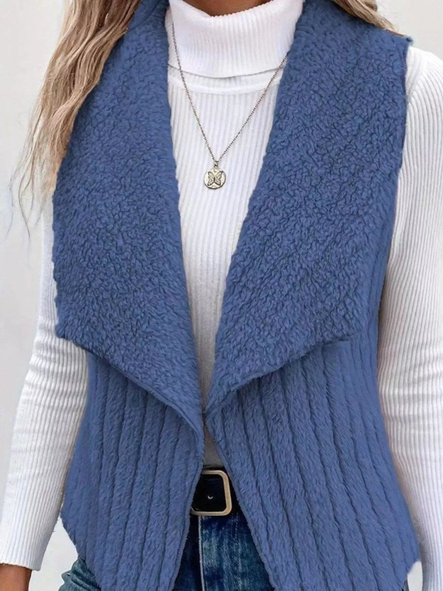 Blue fleece vest with open front and ribbed texture, worn over a white turtleneck.