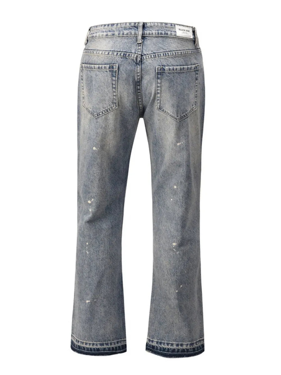 Distressed wash bootcut jeans with raw hem and paint splatters.