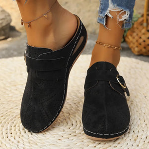 Black laser-cut buckle mule wedges with white stitching and perforated details.