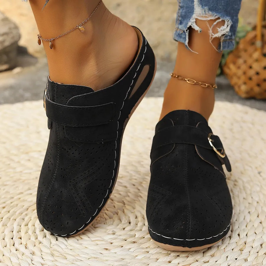 Black laser-cut buckle mule wedges with white stitching and perforated details.