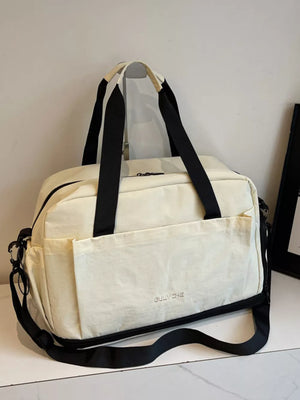 Off-white Oxford cloth travel tote bag with black straps and exterior pockets.