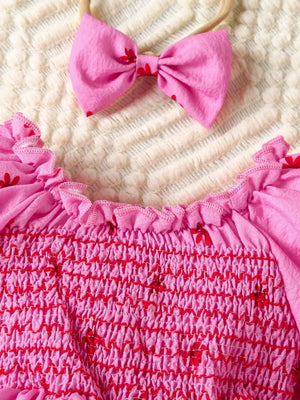 Pink floral smocked baby dress with ruffled neckline and matching bow headband.
