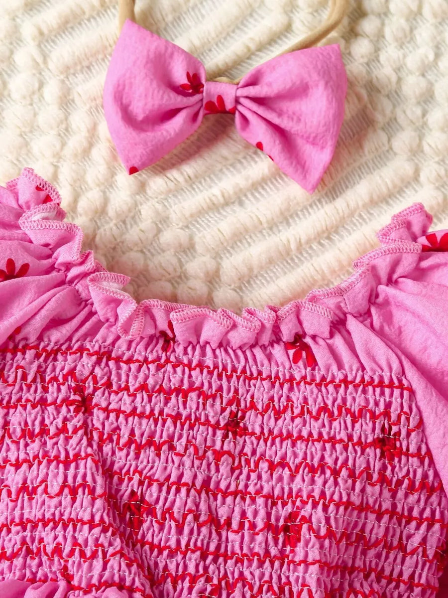 Pink floral smocked baby dress with ruffled neckline and matching bow headband.