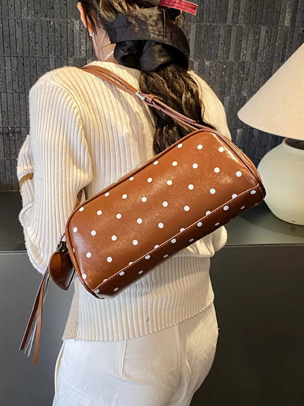 Brown polka dot shoulder bag with adjustable strap and tassel detail.