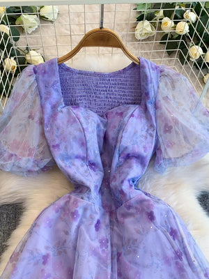 Purple floral maxi dress with sweetheart neckline, smocked bodice, and sheer puff sleeves.