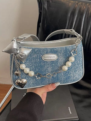 Denim shoulder bag with pearl chain, heart charm, and silver bow detail.