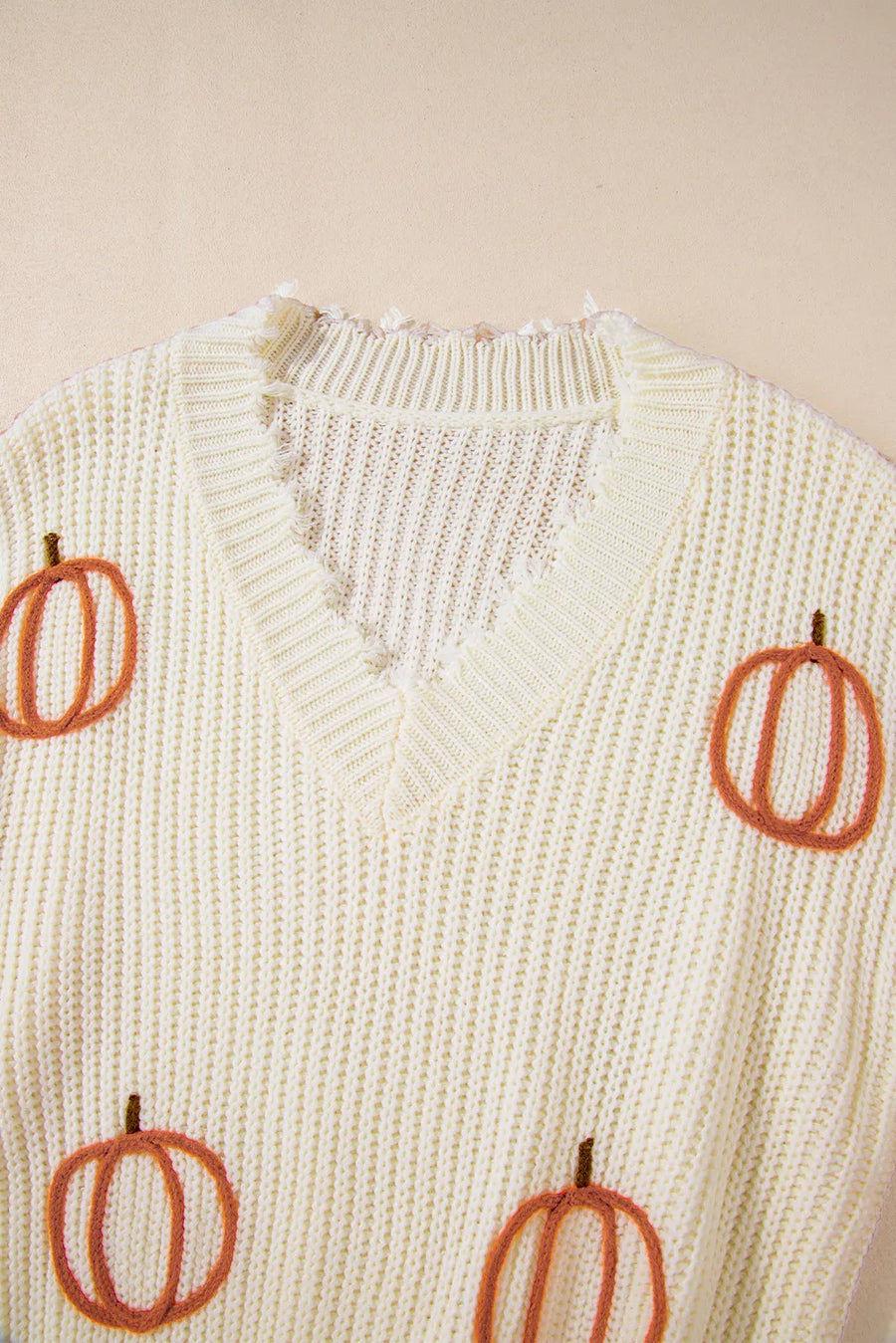 Beige distressed knit sweater with embroidered pumpkins, V-neck, and frayed trim.