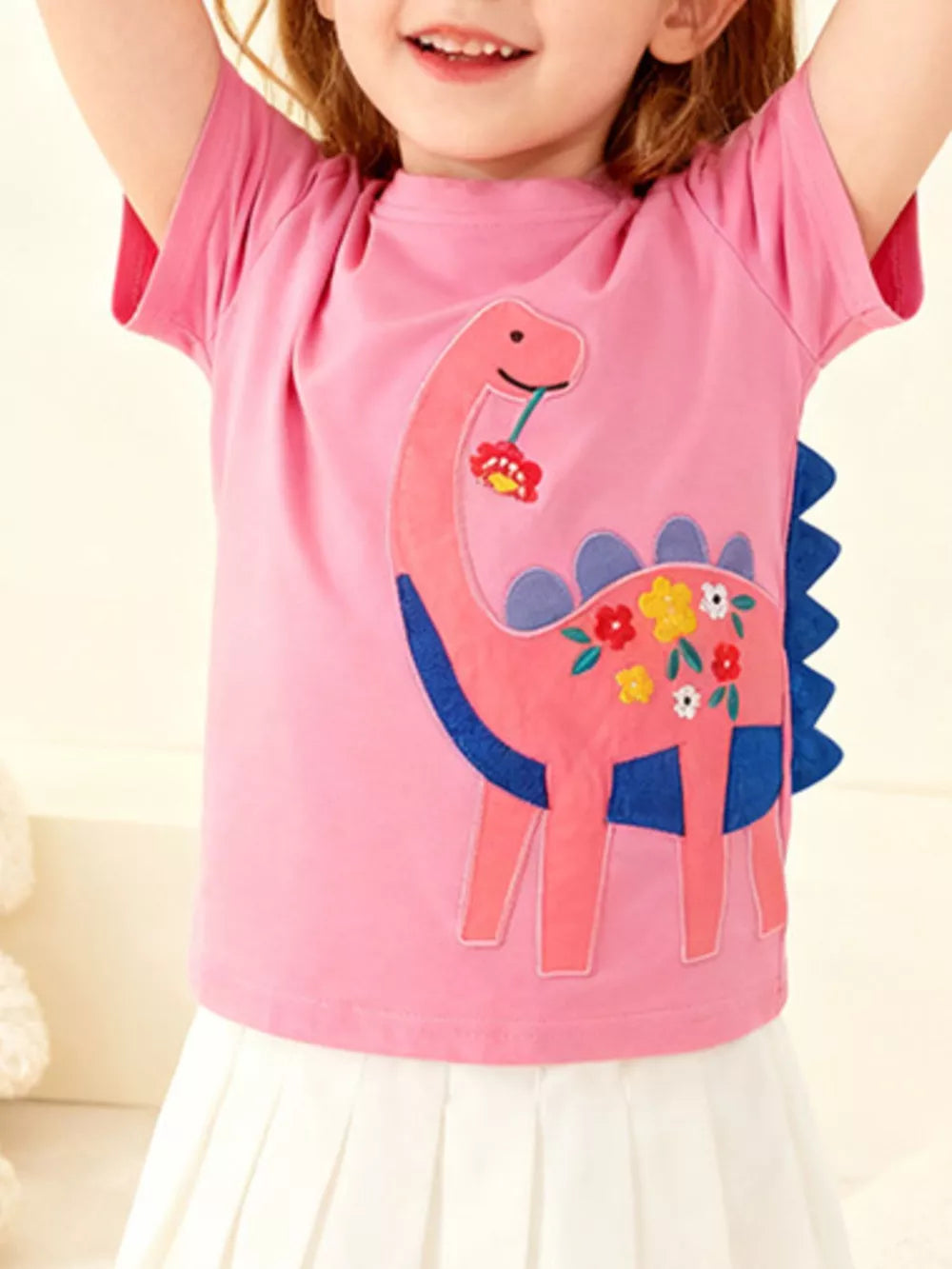Pink cotton t-shirt for kids with a dinosaur embroidered with flowers.
