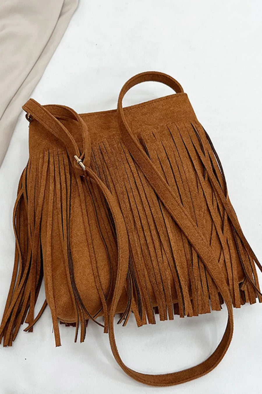 Brown suede crossbody bag with long fringe detail and adjustable strap.
