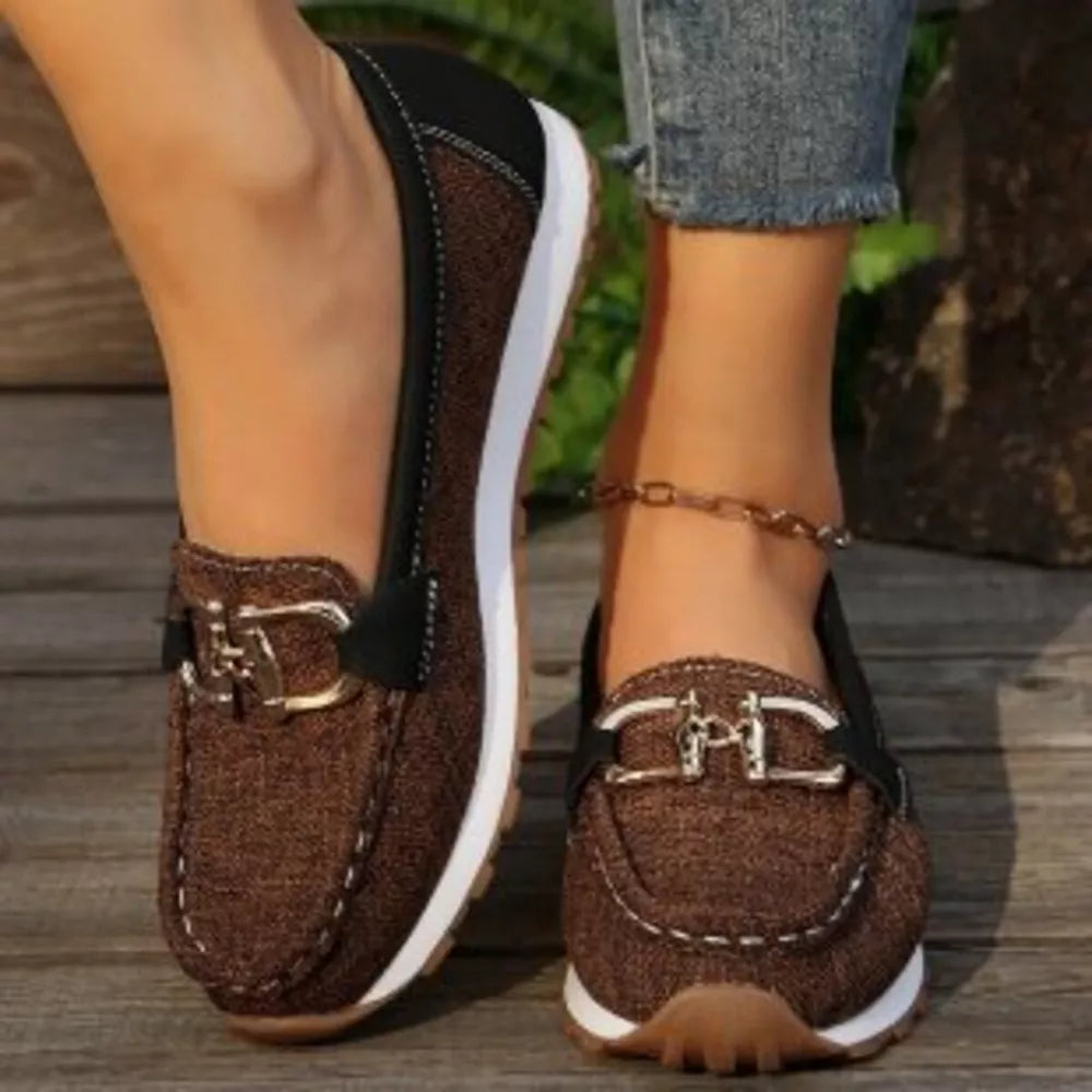 Brown round toe slip-on loafers with decorative buckle detail and white stitching.