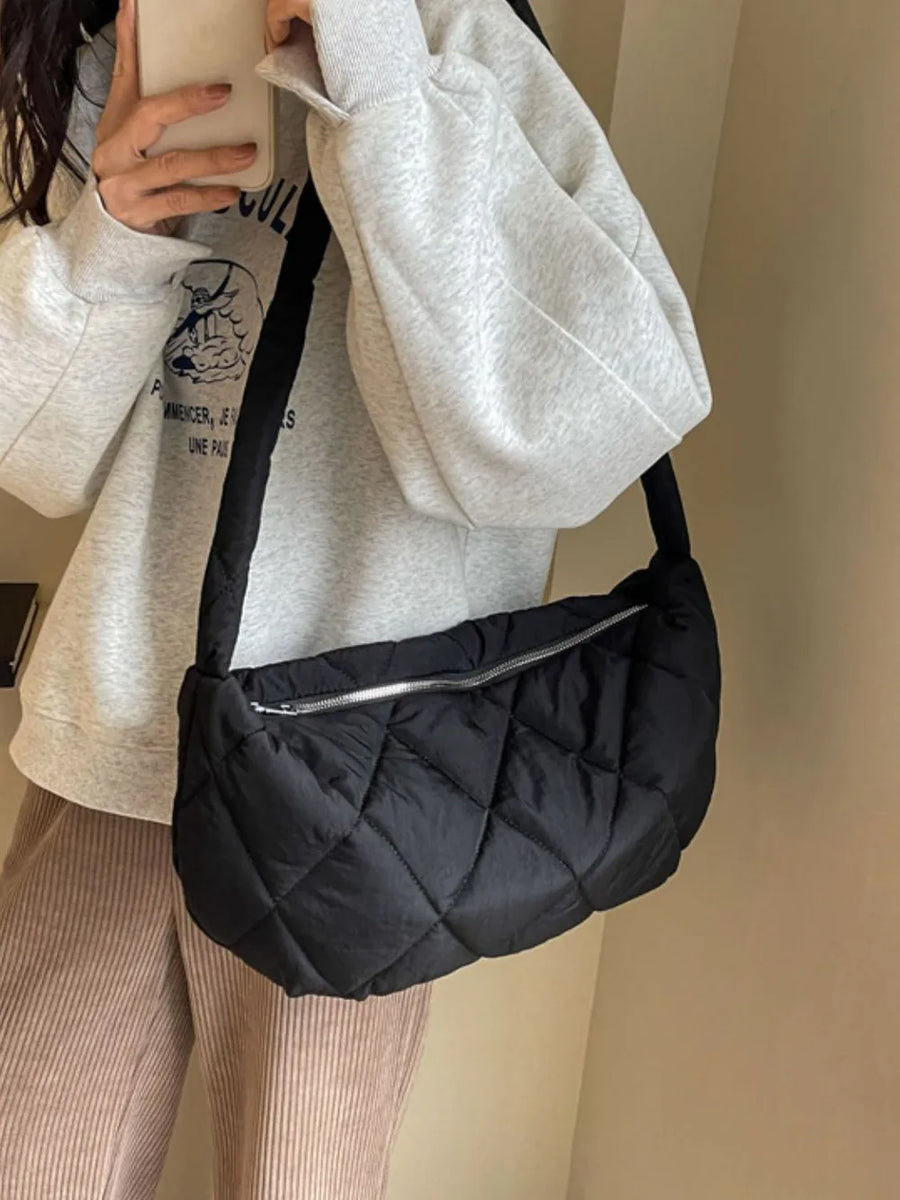 Black quilted crossbody bag with silver zipper detail and adjustable strap.