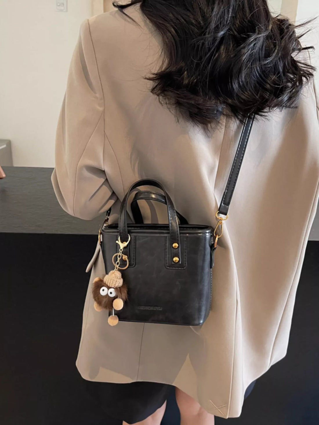 Black leather crossbody bag with top handles and a cute charm detail