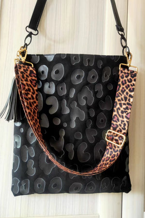 Black crossbody bag with embossed leopard print, tassel, and leopard print strap.