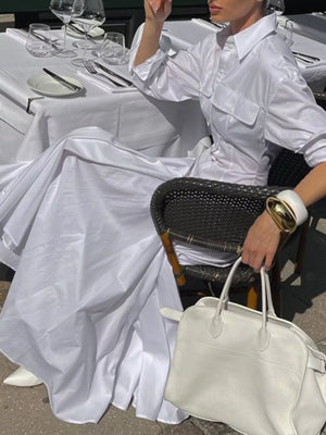 White oversized shirt dress with voluminous skirt and two chest pockets, styled with white pointed-toe heels and a white