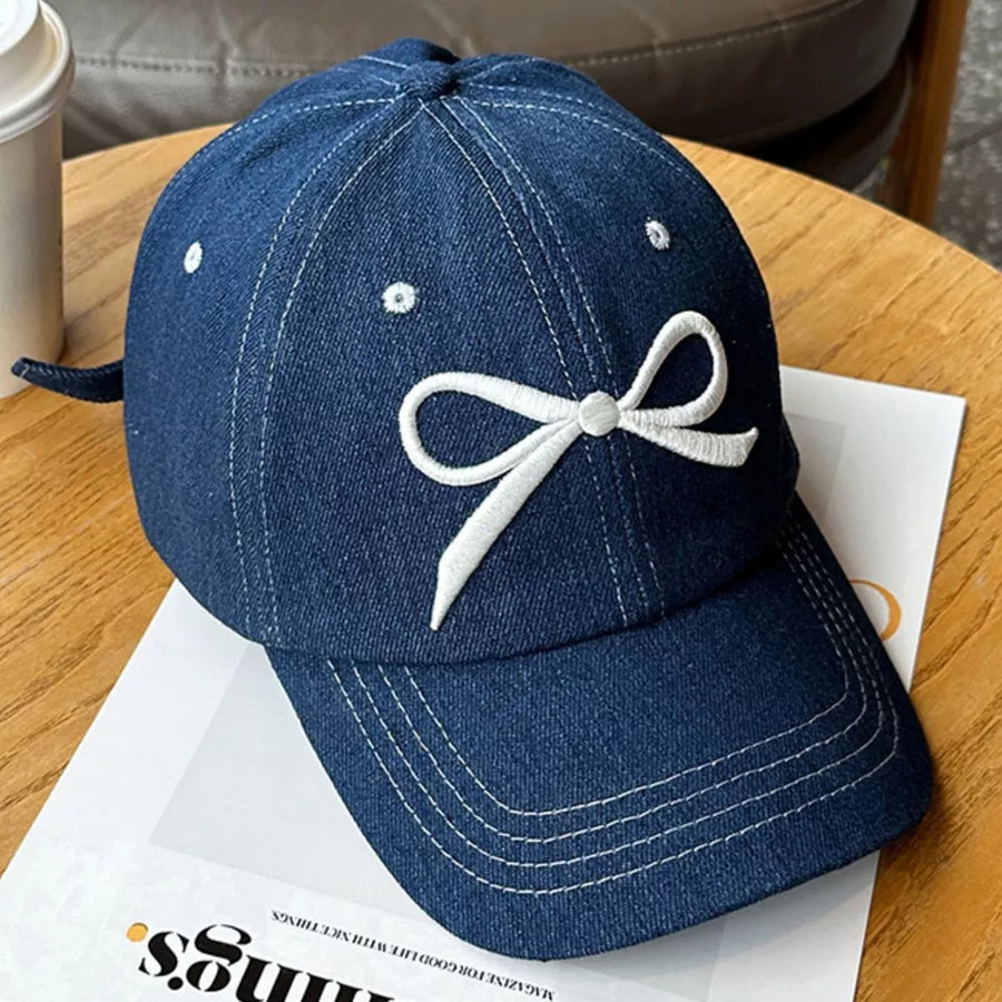 Dark blue denim baseball cap with white embroidered bow accent and contrast stitching.
