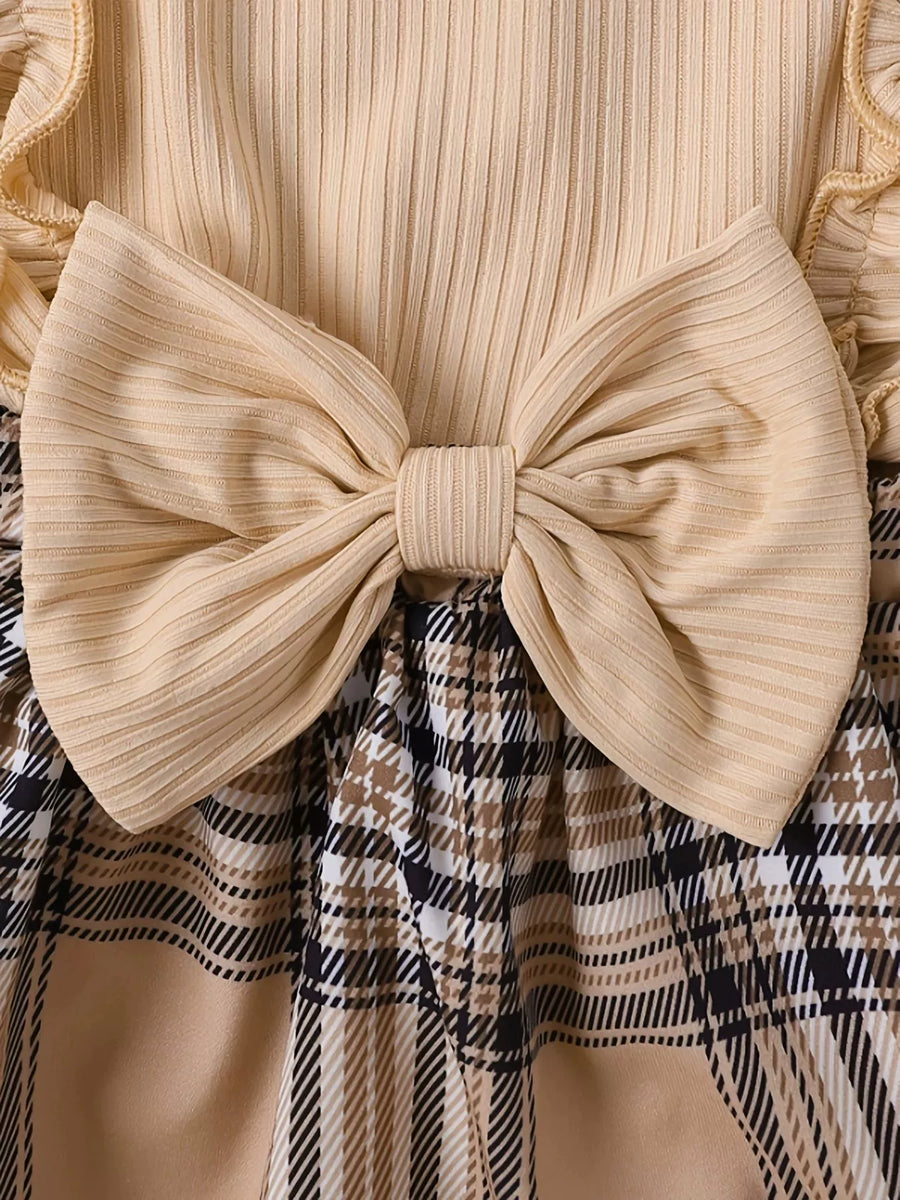 Baby bodysuit with ruffled trim and large bow, paired with a plaid skirt.